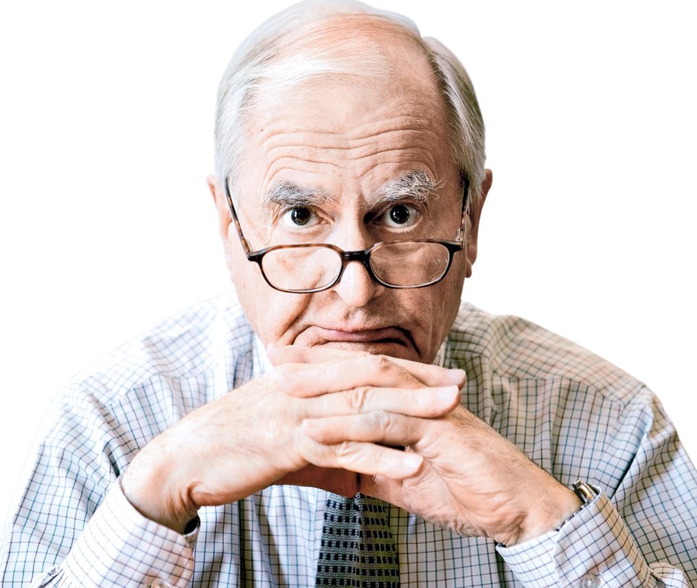 An older white man wearing glasses stares directly into the camera with his hands under his chin