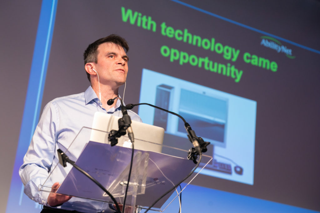 Robin Christopherson stood in front of a presentation, screen reads 'with technology came opportunity'