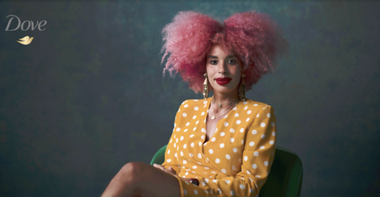 Dove campaign image of a stylish woman in a yellow spot dress with pink Afro hair